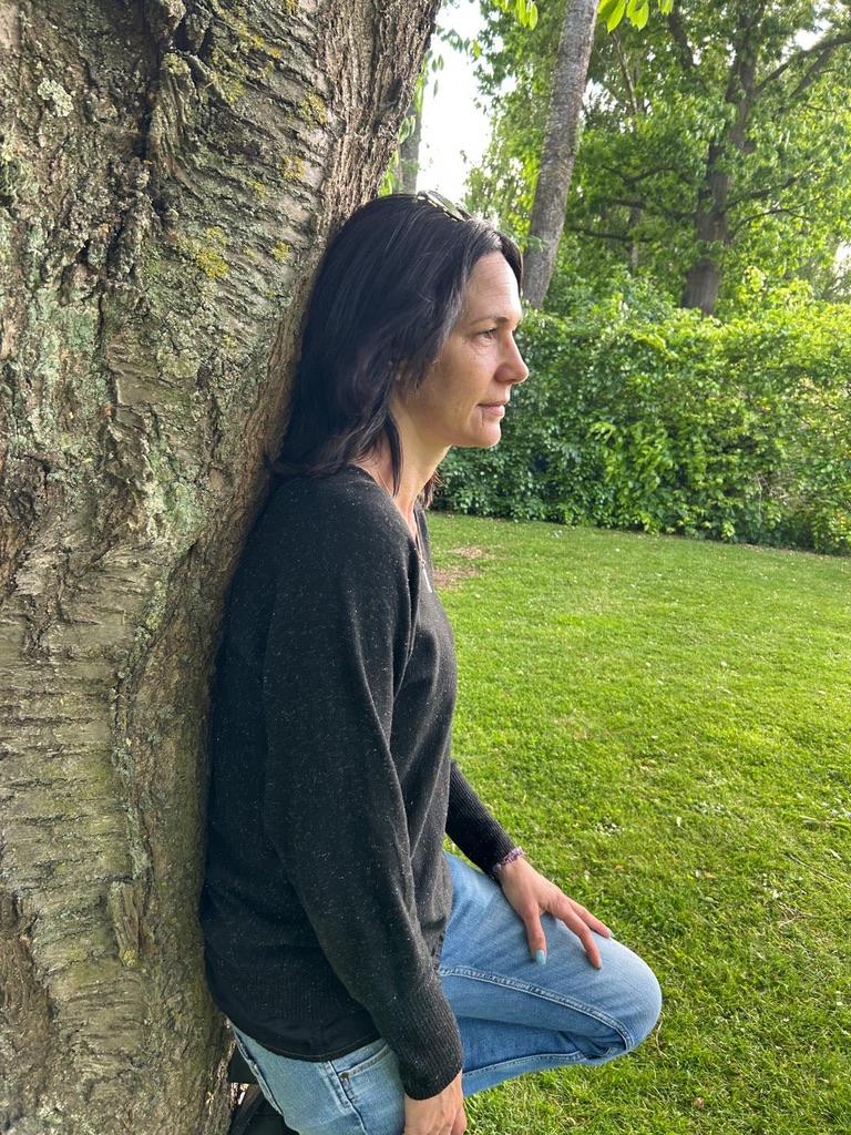 Corentine appuyée contre un arbre, regard au loin, jardin