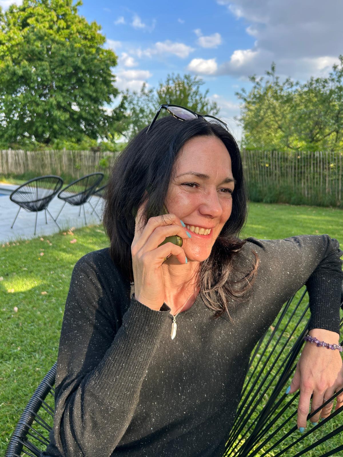 Corentine souriante, téléphone à l’oreille, assise à l’extérieur